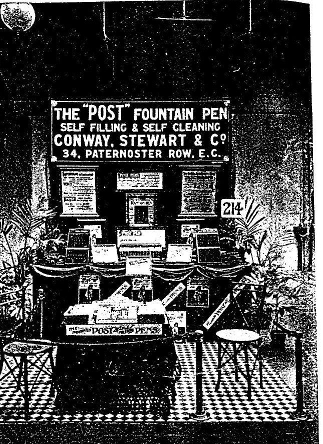 A grainy black and white photograph of a small exhibition stand with a large painted signboard reading THE POST FOUNTAIN PEN, SELF FILLING AND SELF CLEANING, CONWAY, STEWART AND CO, 34 PATERNOSTER ROW, E.C., with display cards and potted palms below.