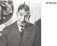 A black and white photograph of a middle-aged man in a suit seated at a desk, looking towards the camera.