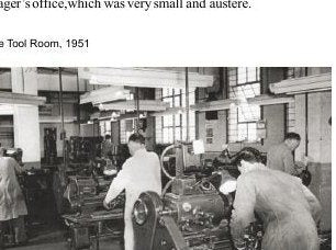A black and white photograph of men in white work coats standing at rows of machine tools in a bright workshop bay.