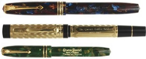 Three capped fountain pens laid horizontally one above another, the top in mottled amber and brown, the middle in dark ebonite with a gold cap band, the lowest in pale green marbled casein.